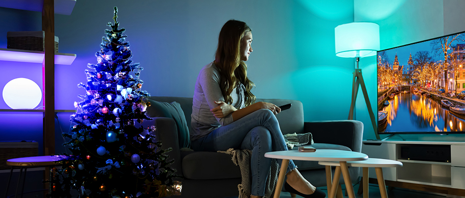 Νεαρή γυναίκα κάθεται στον καναπέ βλέποντας ταινία στην τηλεόραση στο σπίτι και ο χώρος έχει Χριστουγεννιάτικη διακόσμηση